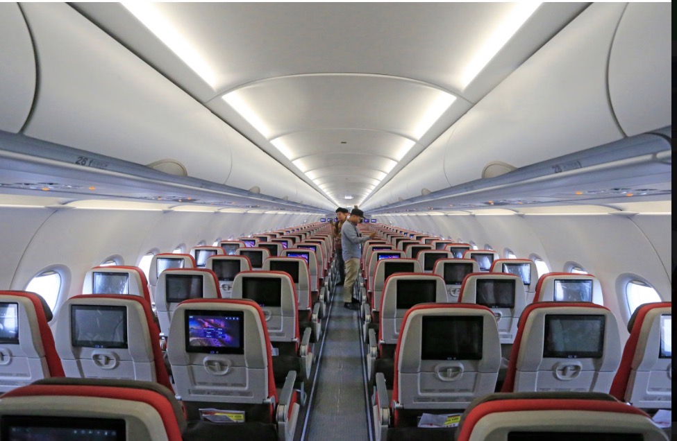 Interior de una cabina de avión con filas de asientos y pantallas individuales