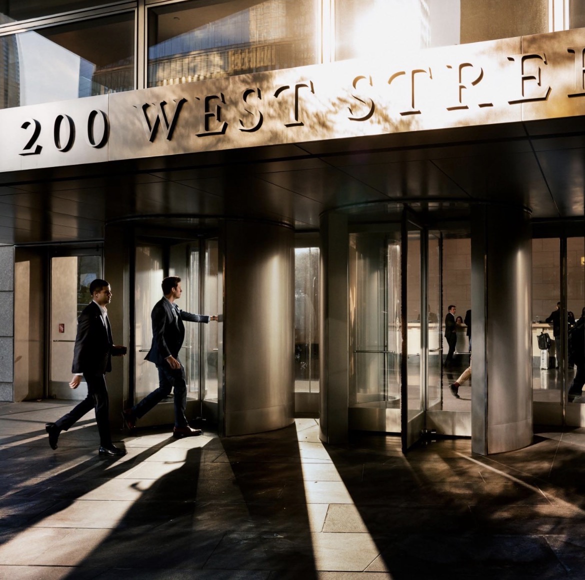Entrada del edificio de 200 West Street con puertas giratorias y personas caminando
